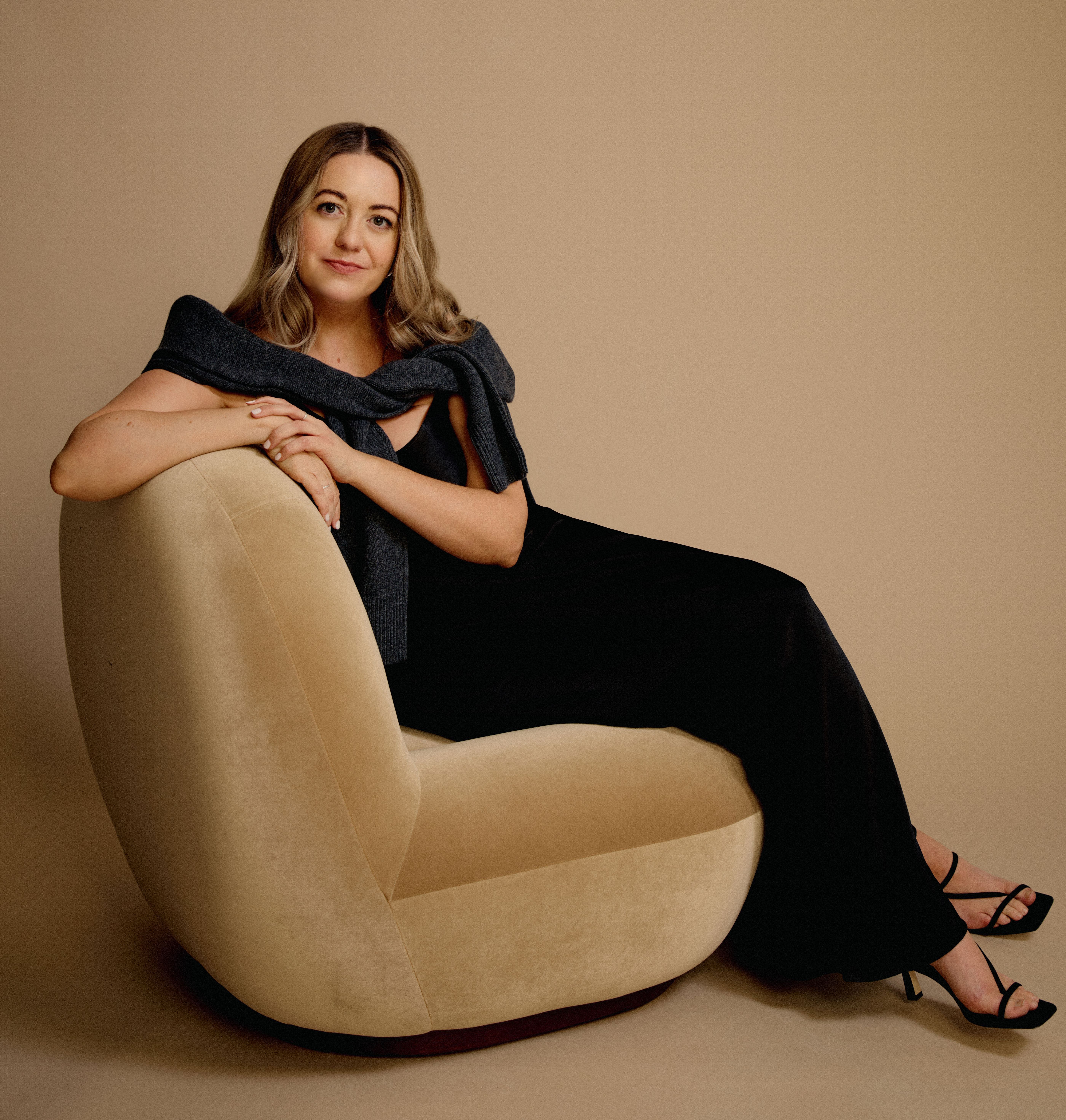 Franky Rousell sitting on a cream-colored chair against a beige background.