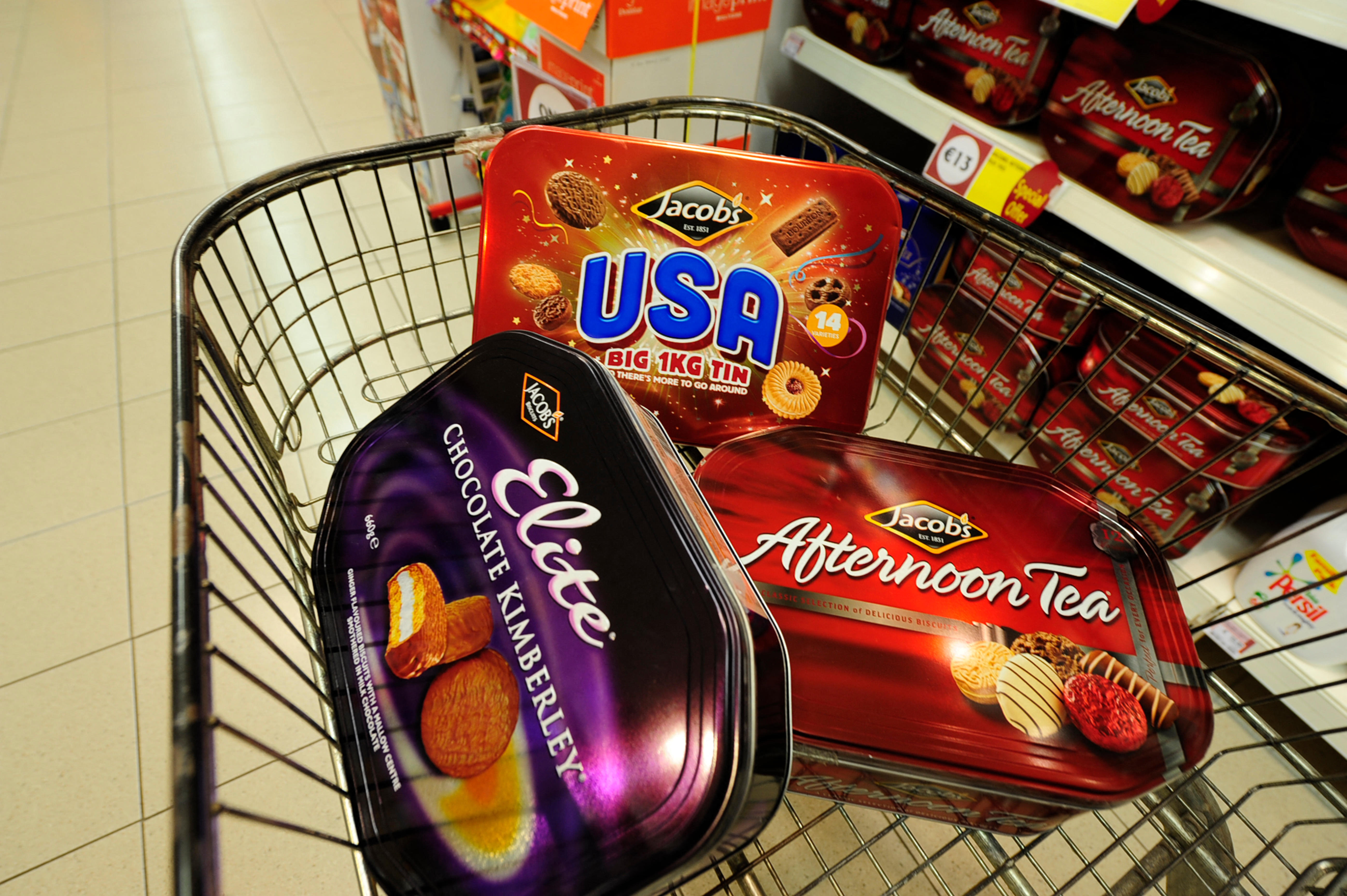 A shopping trolley filled with three different Jacob's biscuit tins: USA, Chocolate Kimberley, and Afternoon Tea.