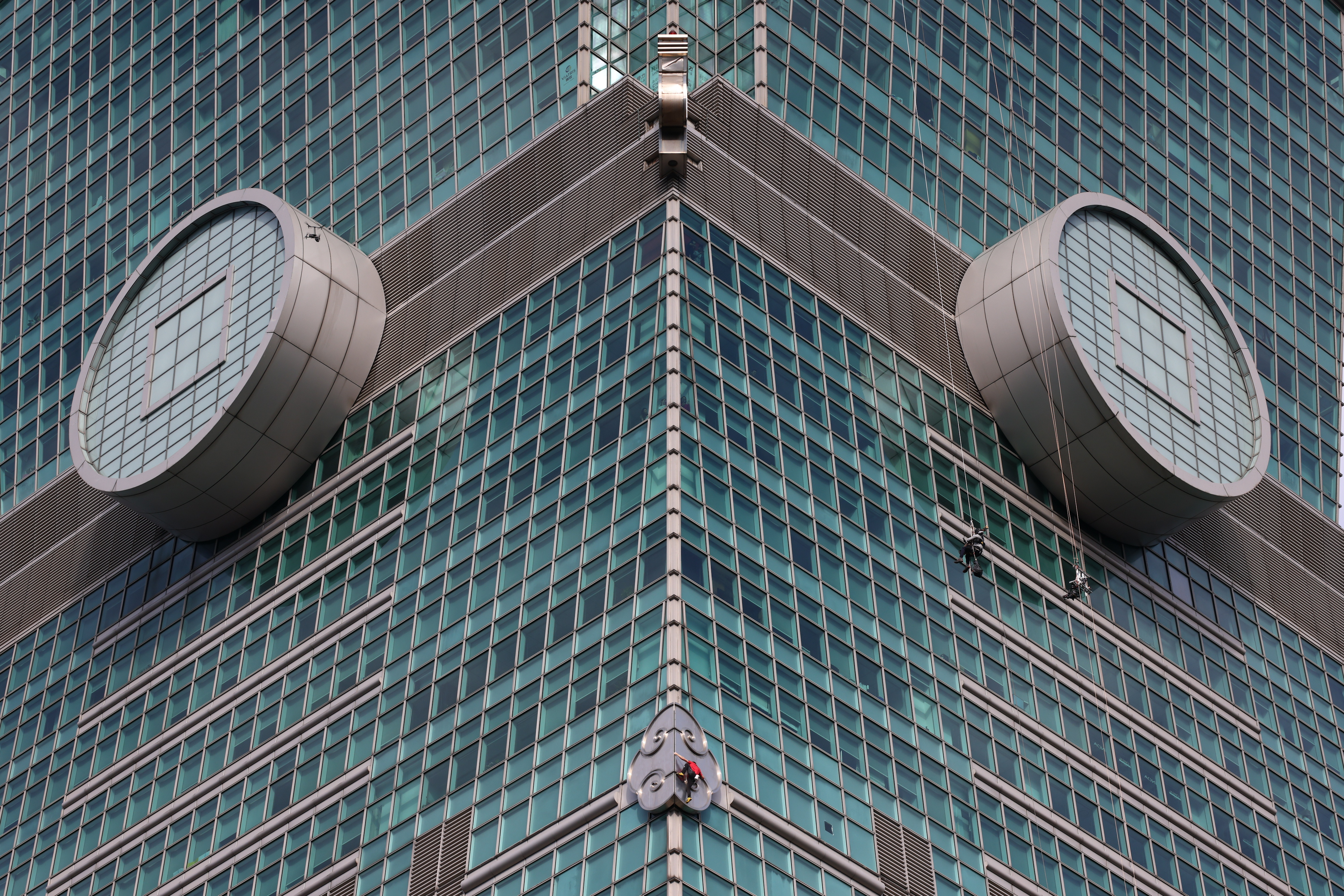 Alex Honnold climbing the Taipei 101 skyscraper, with two other climbers rappelling nearby.
