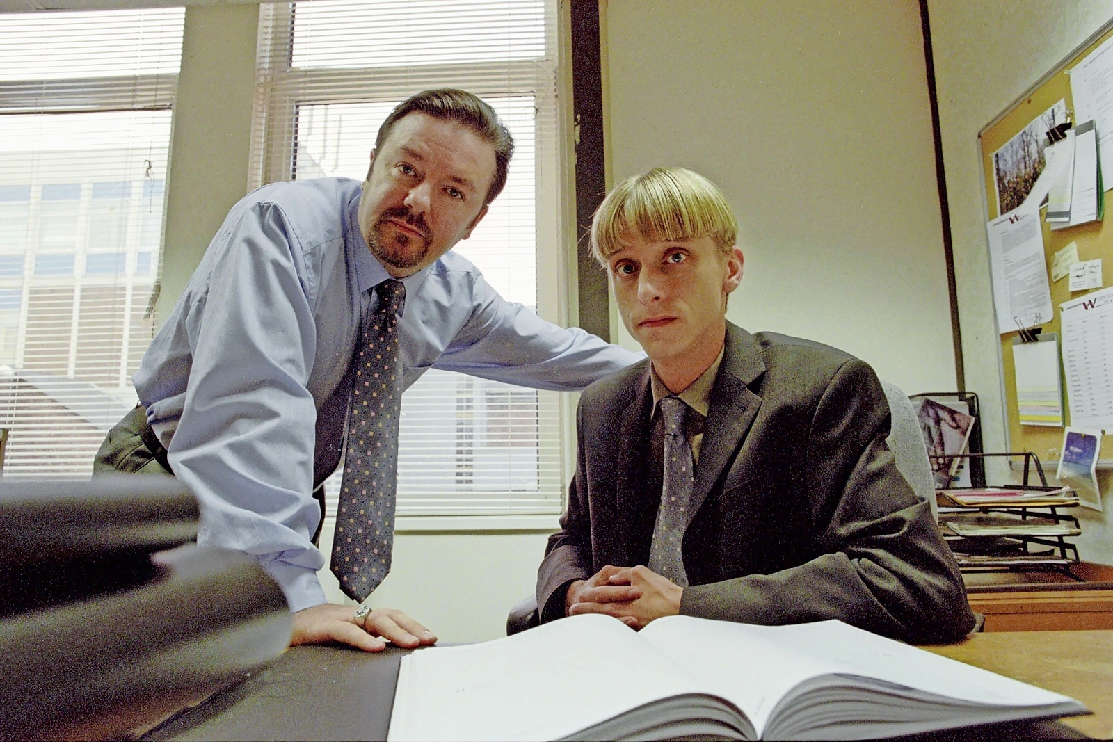 David Brent (Ricky Gervais) leaning over Gareth Keenan (Mackenzie Crook) at his office desk.