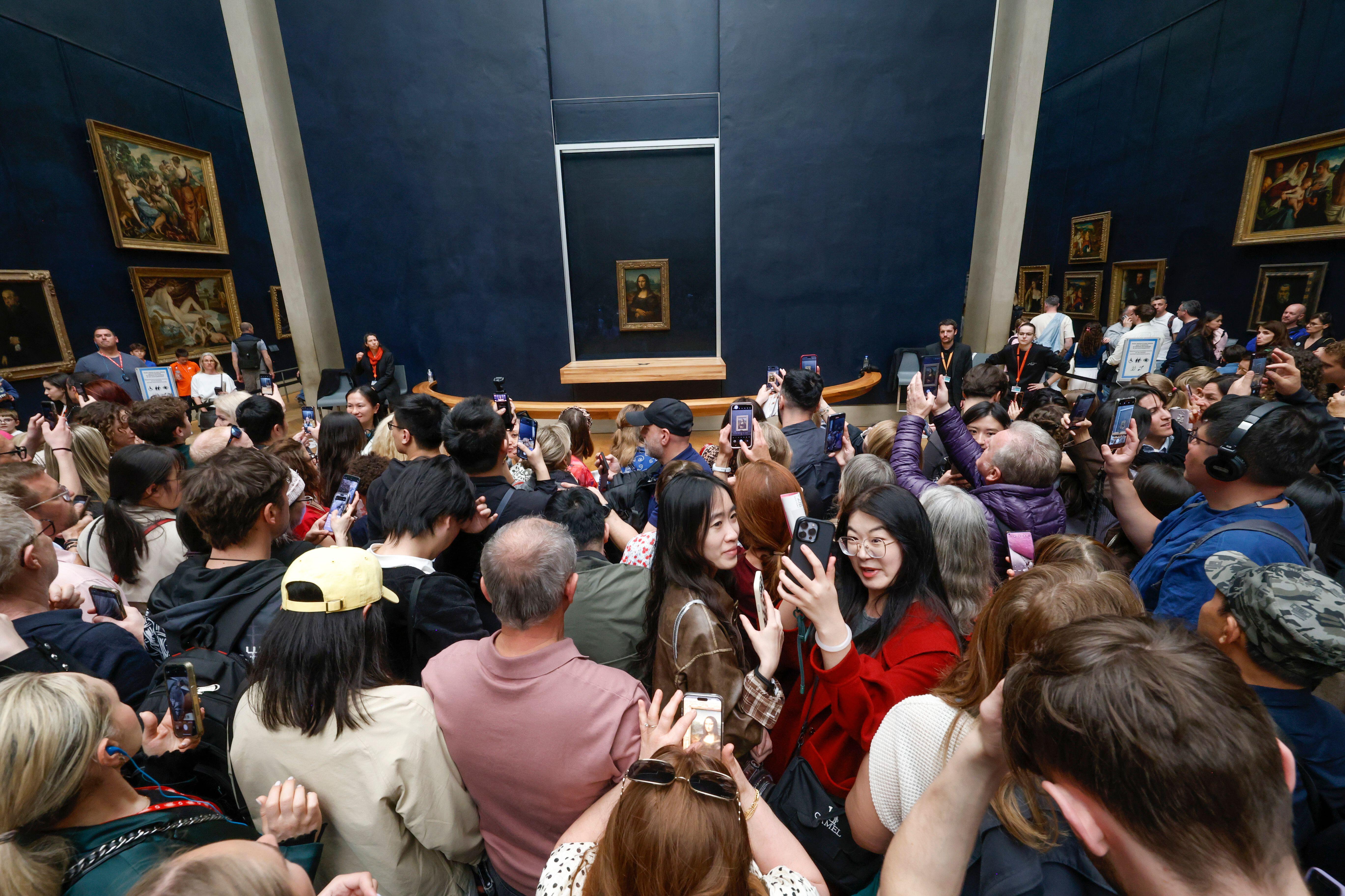 Large crowd of people taking photos of the Mona Lisa in the Louvre Museum.