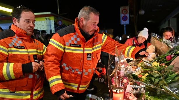 Firefighters gather to leave flowers and candles at the scene at Le Constellation bar