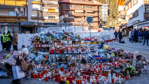 hundreds of flowers, candles at a makeshift memorial with police and other people standing in the backgrounds