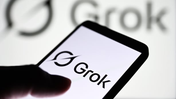 A Grok logo of a generative artificial intelligence chatbot developed by xAI is seen on a smartphone and in the background