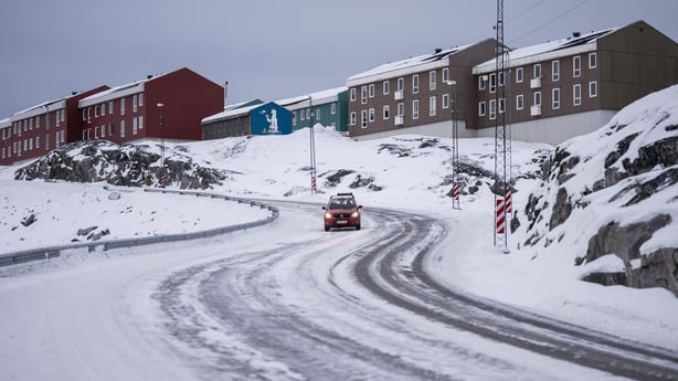 A car drives down a snow-covered road past residential buildings in Nuuk, Greenland