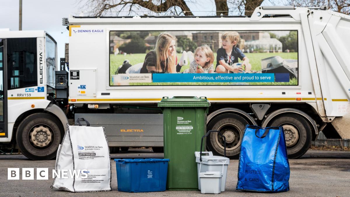 White waste bin lorry with green wheeler bin and other recycling containers in front of it including a white bag, a blue bag, a blue box, a grey caddy and a smaller grey caddy.
