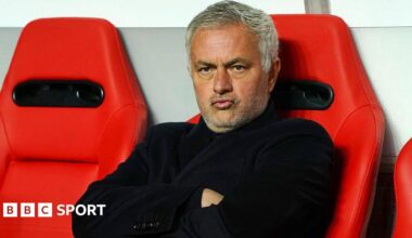 Jose Mourinho purses his lips and cross his arms as he sits on a red chair