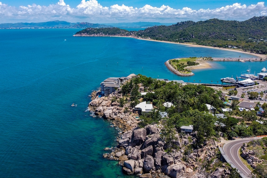 A drone shot of blue waters surrounding an island, with greenery and a number of structures on it.