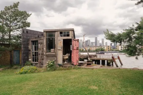 Master Shipwrights House Green grass in foreground, shed in background with river beyond that