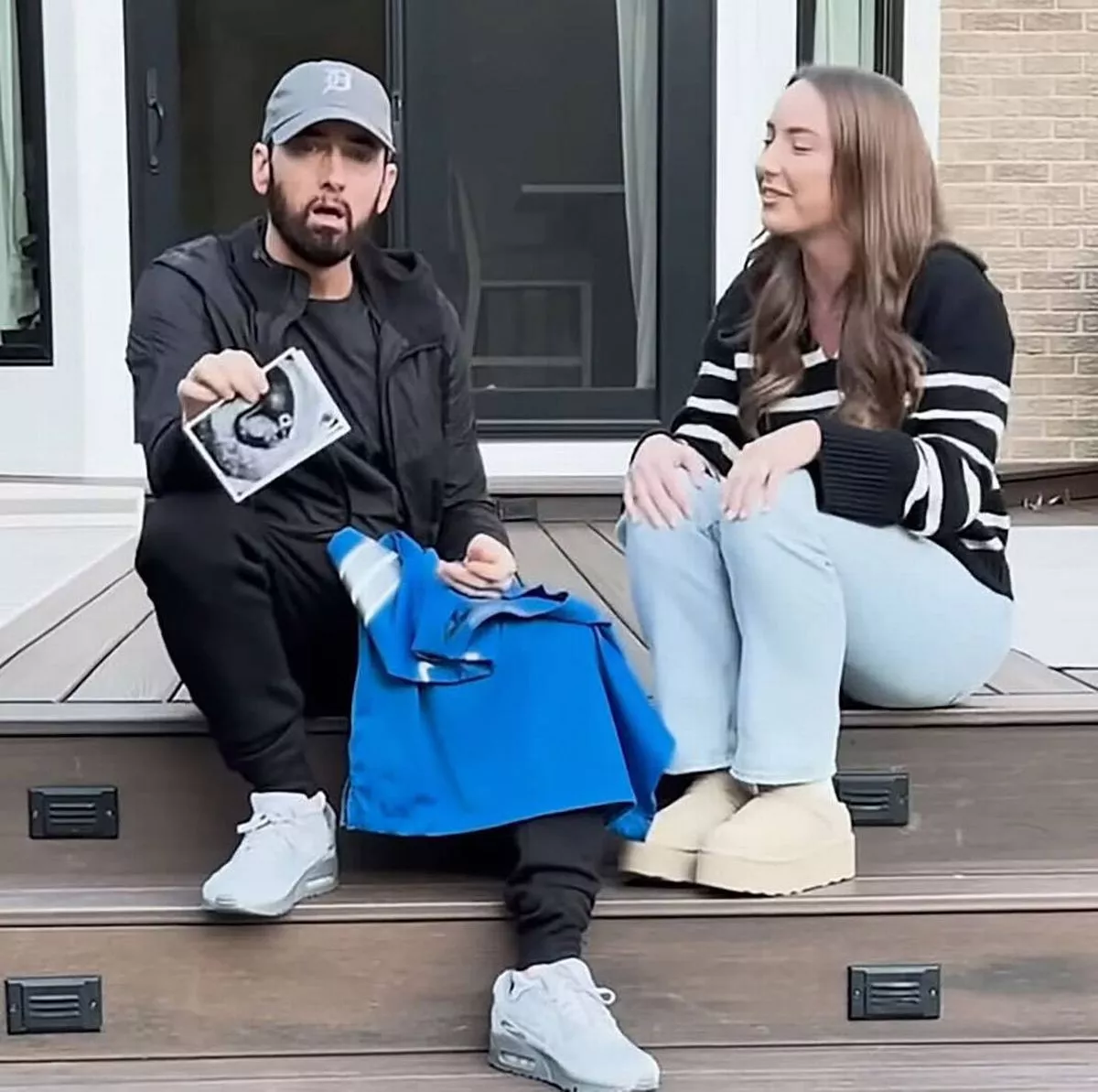 Eminem sat on a porch holding up a baby scan photo with a blue jersey on his knee, alongside his daughter Hailie Jade Scott Mathers.