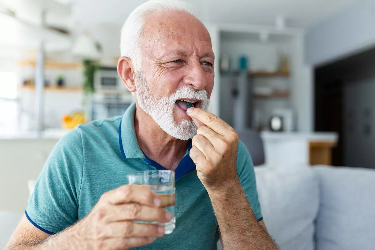 Senior man takes pill with glass of water in hand