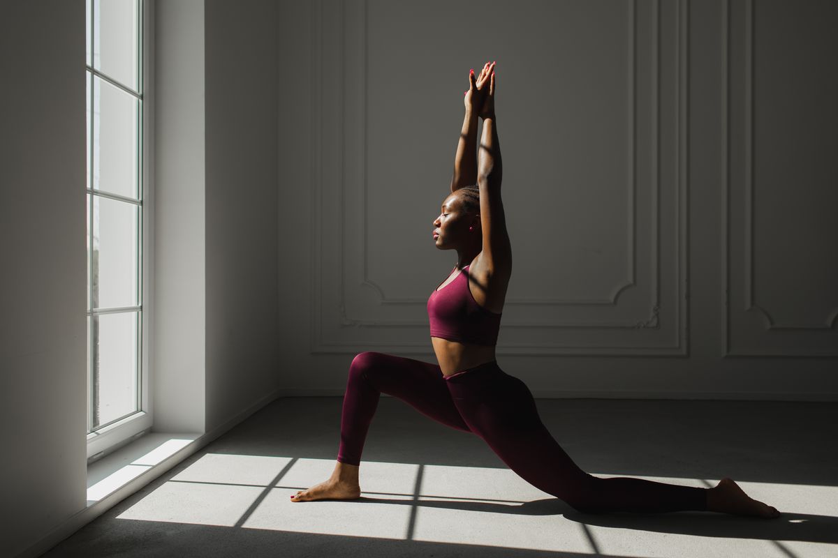 woman with braided hair practicing yoga and doing variation of High Lunge, version of Virabhadrasana I (Warrior I Pose).