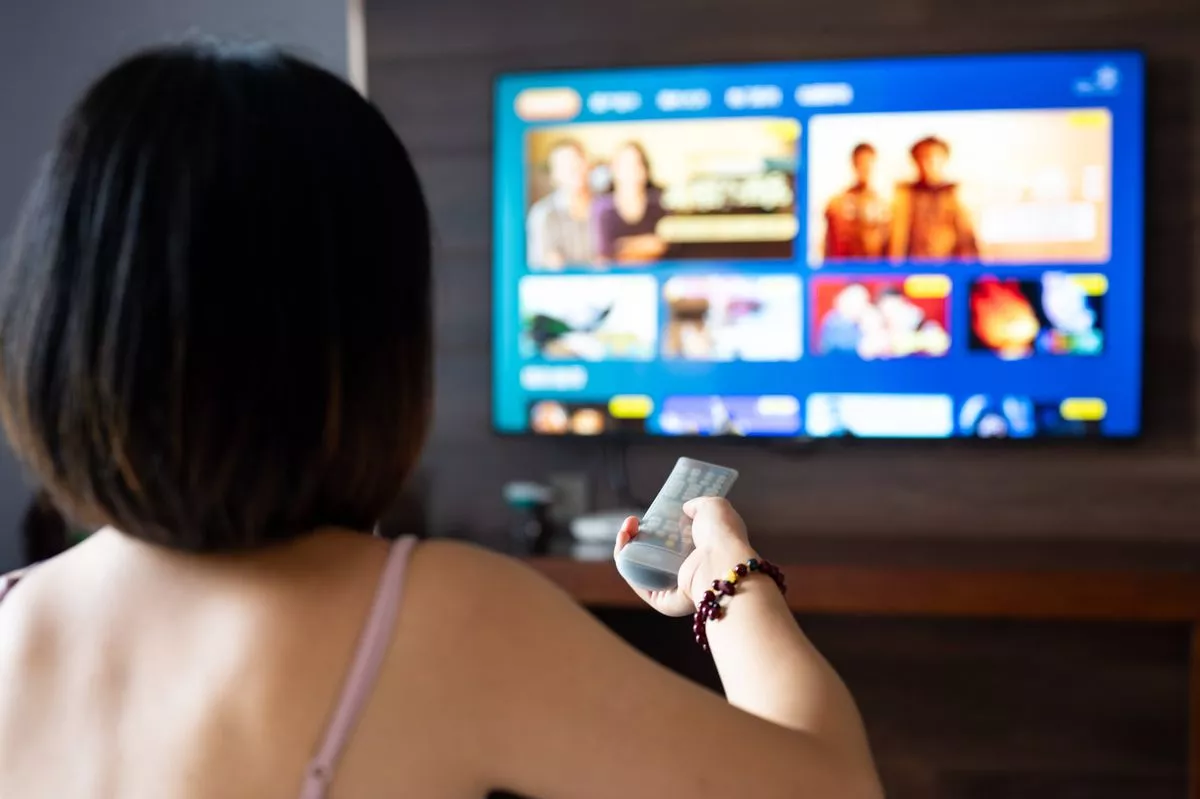 Close up of a person holding a control remote with a television screen on the background