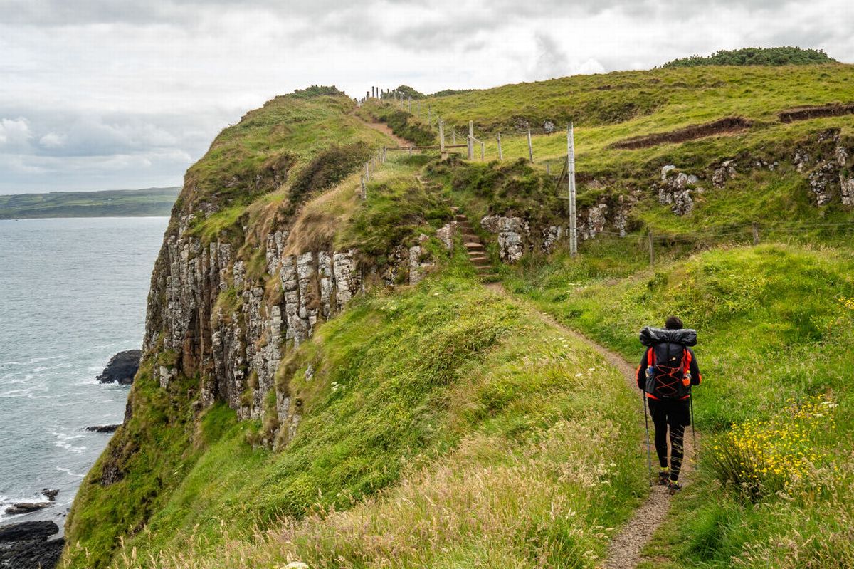 A hiker seen walking next to the edge of a cliff at the Causeway Coast in Northern Ireland