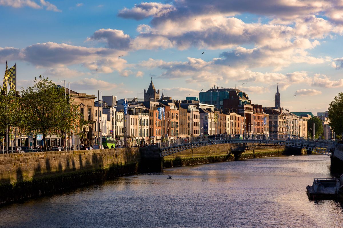 Dublin, Ireland - June 8, 2024: Pedestrians cross the  Ha'penny Bridge over the River Liffey in Dublin, at sunset.