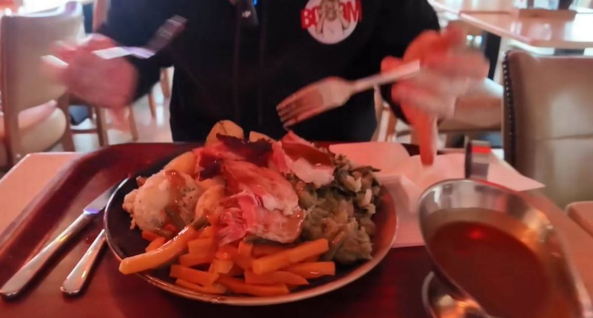 A dining setting featuring a plate of diverse food items, including meat, vegetables, and sauce, with a person using a fork.