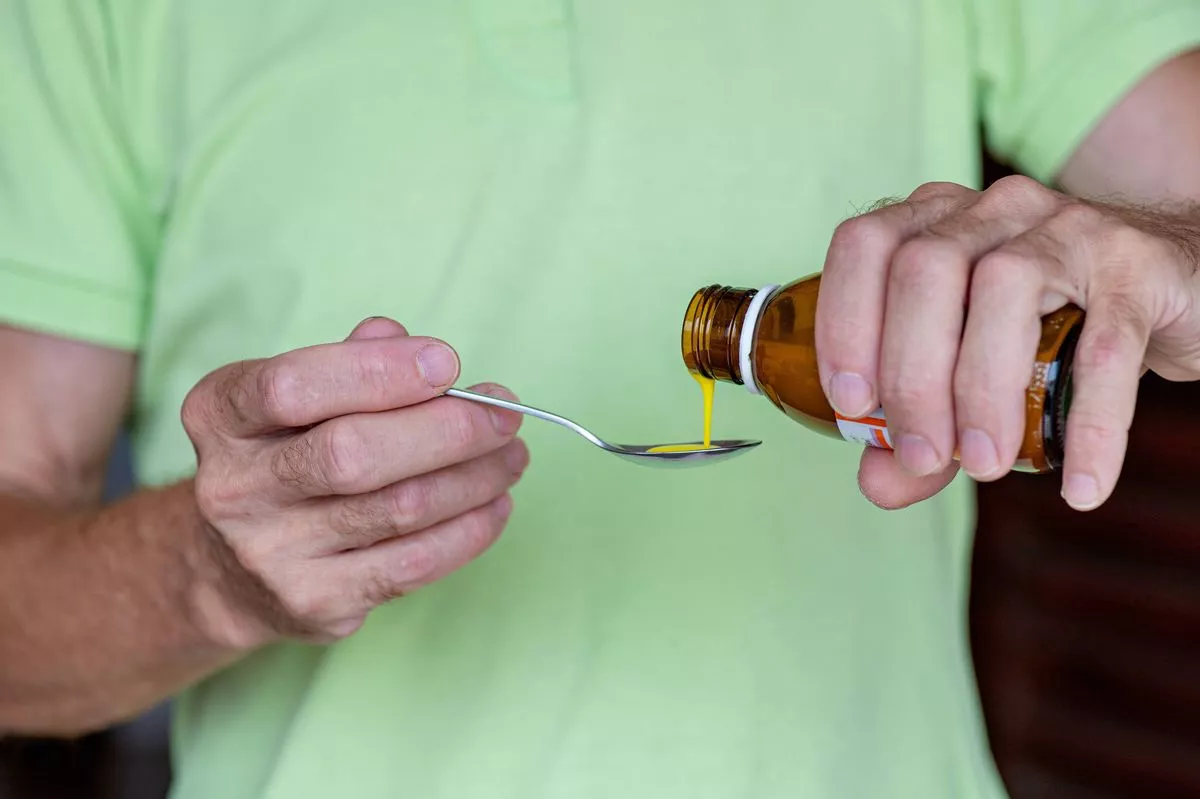 Male hands carefully pouring syrup-like medicine into a metal spoon. Concepts: home treatment, accurate dosage, family care, child and adult healthcare.