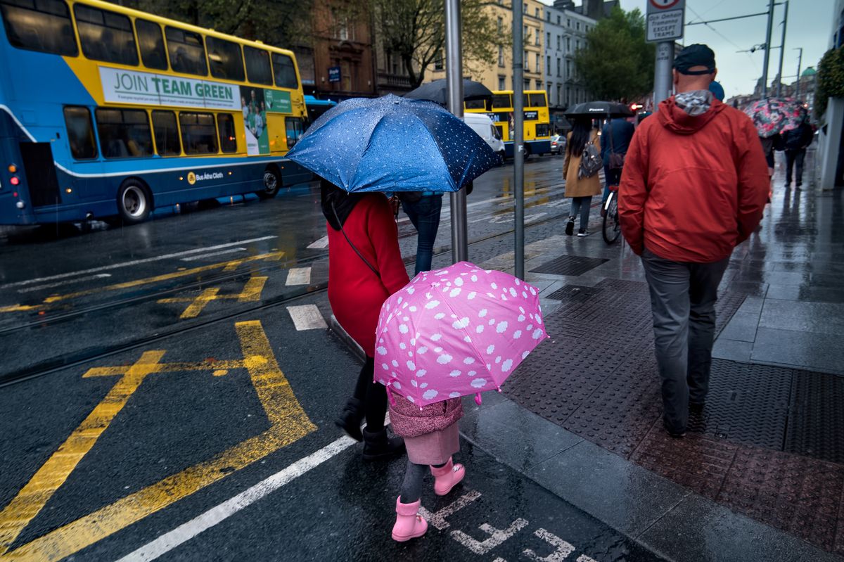 Dublin, Ireland - 05/27/2019:  Mother and daughter using polka dotted umbrellas during a rain shower as they cross a street in Dublin, Ireland.