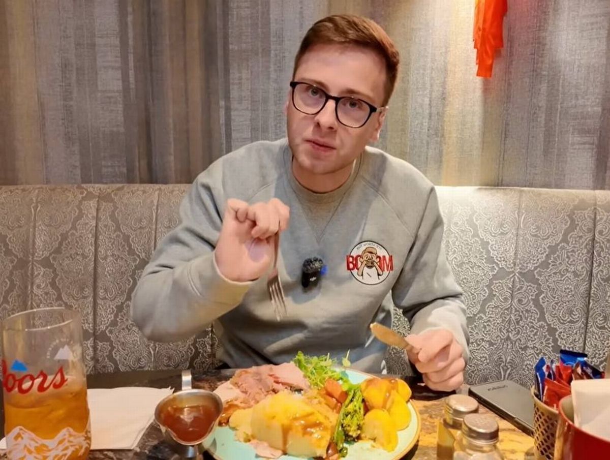 An individual is seated at a table, actively engaged in the act of consuming a meal. The setting appears to be a casual dining area, with various food items and beverages present on the table. The individual is dressed casually and appears to be in the midst of savoring their food.