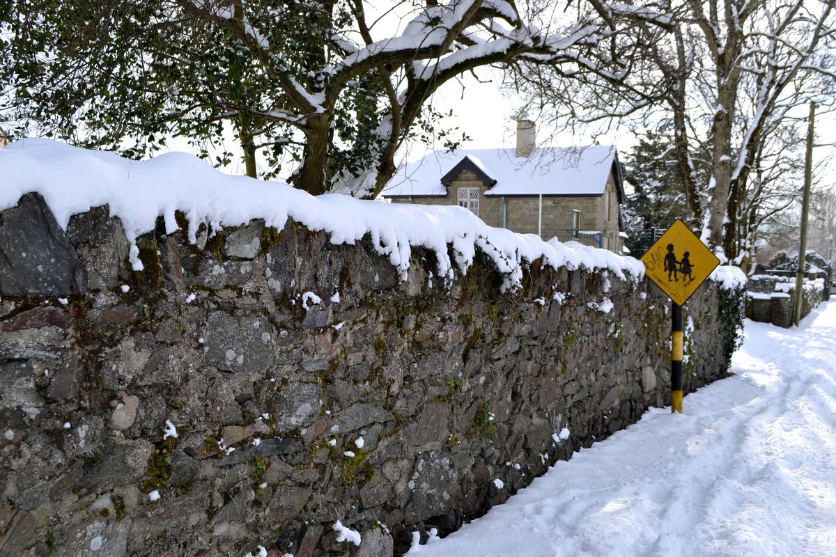 A children crossing sign on a snow covered lane in rural Ireland.  The road is empty because school has been cancelled due to heavy snow.  Rural Ireland slows down on a snowy day.