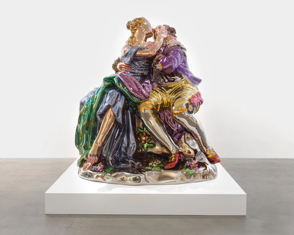 Colorful porcelain sculpture of a couple kissing, dressed in Renaissance-style clothing, displayed on a white platform.
