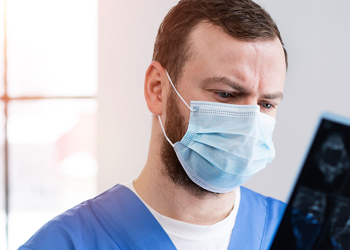 Doctor in blue scrubs wearing a face mask closely examining medical scans focused on unprofessional things doctors say.