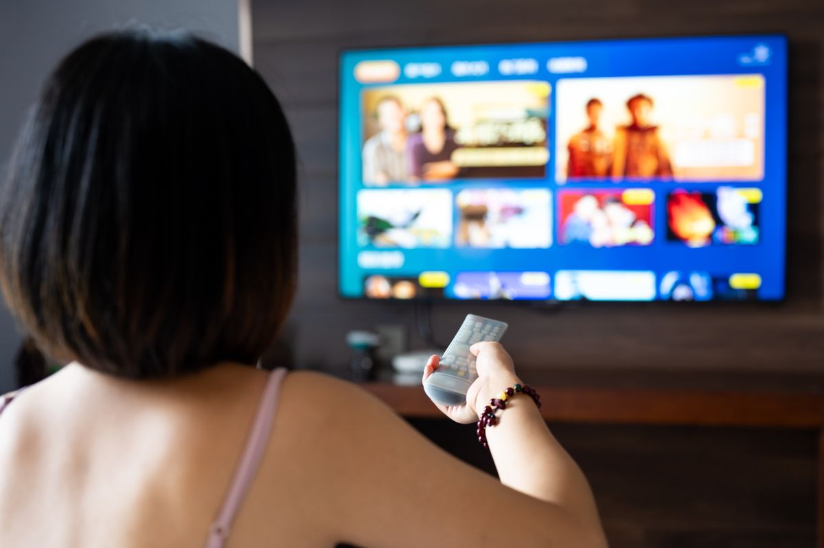 Close up of a person holding a control remote with a television screen on the background
