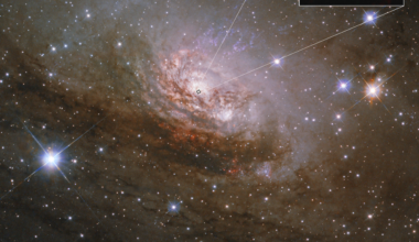 Image shows a large spiral galaxy that that has a bright white center, with several lanes of reddish-brown dust and gas in between faint white arms. The galaxy takes up the center third of the frame. There are several thousand stars, some with diffraction spikes, scattered around the image. This image is labeled Hubble. A small box outlining an area at the center of the galaxy leads a pullout square at the top right. The image, labeled Webb, is dark with a white glowing oval at the center.