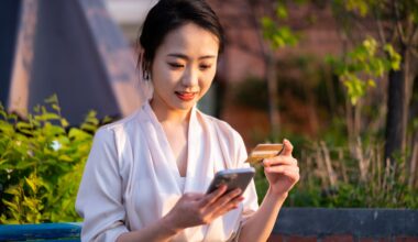 Asian young woman sitting on chair, paying with smart phone in city public park stock photo