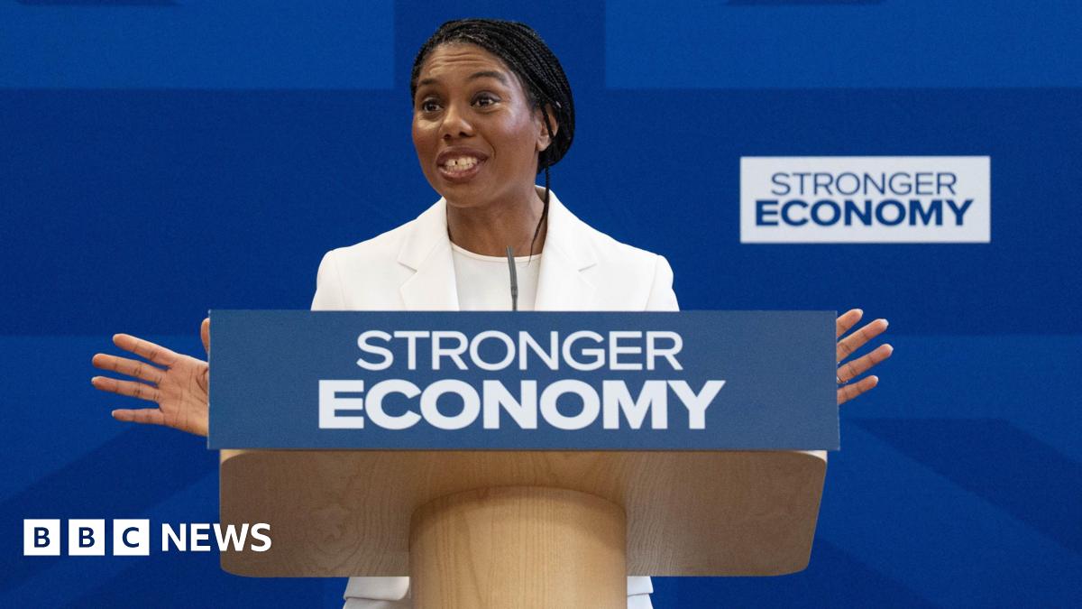 Conservative Party leader Kemi Badenoch gives a speech from behind a podium reading "stronger economy" in front of a blue backdrop.