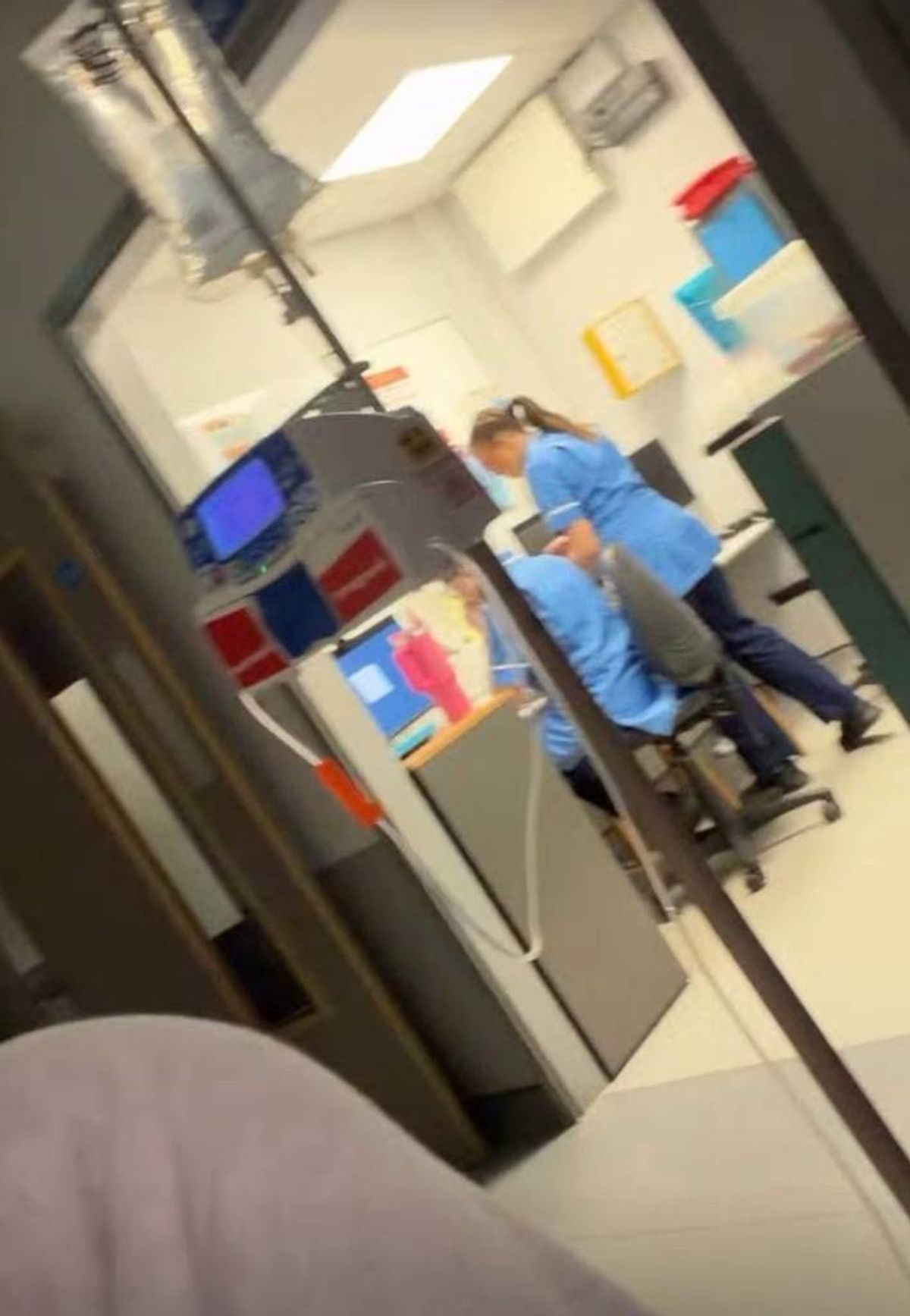 In a modern medical facility, a healthcare professional, dressed in a blue scrub suit, is diligently attending to a patient. The setting is well-lit, with various medical equipment and supplies visible in the background, indicating an environment focused on patient care and medical procedures.