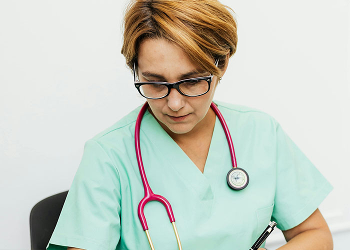 Female doctor in green scrubs and glasses with a stethoscope, writing notes about unprofessional things doctors said to patients.