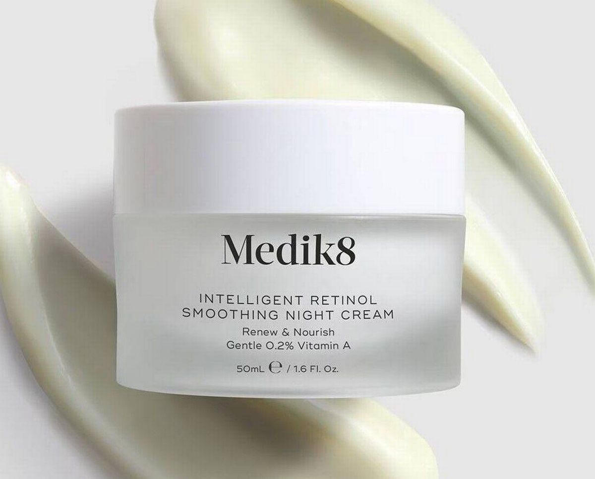 A white cylindrical container labeled "Medik8" with the brand name prominently displayed, positioned on a textured, light-colored background. The product is presented in a cream or lotion form, designed for skincare purposes.