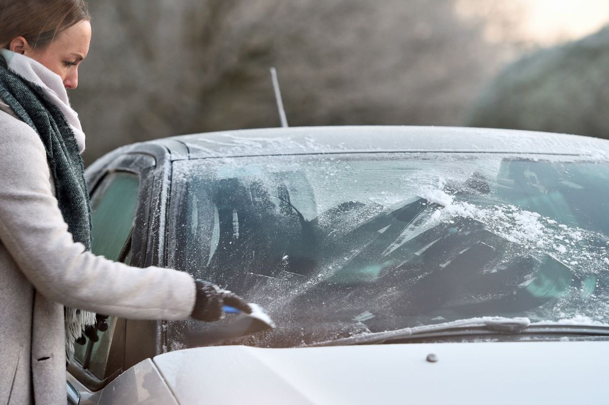 A woman scrapes the windscreen to remove frost from her car (stock image)