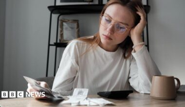 Woman, with her head resting on her hand, looks at receipts while sitting at a table with a teacup and calculator in front of her.