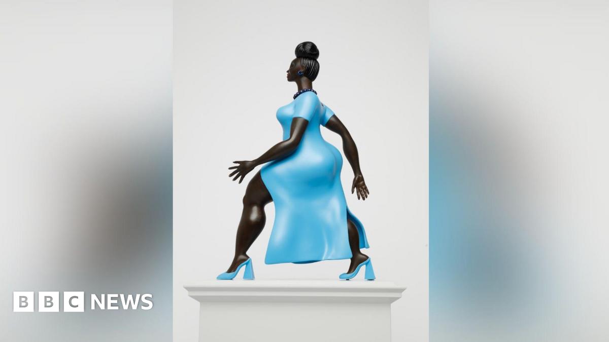 A statue of a woman of colour wearing a striking baby blue dress with matching high heels of the same colour. She has her hair up in a bun and is wearing a black beaded necklace. She is walking with purpose with one arm in front of the other.