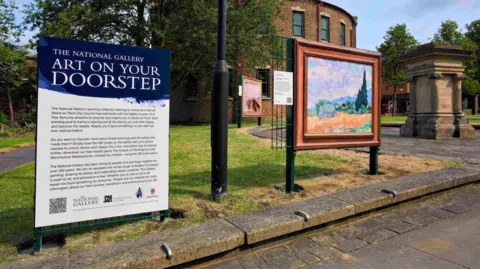 Stoke-on-Trent City Council An interpretation board next to a replica artwork. The board has a dark blue top with white writing that reads The National Gallery Art on Your Doorstep. The artwork and board have been installed on a patch of lawn 