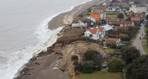Jamie Niblock/BBC A drone image of the coastline at Thorpeness. A large part of the coastline has been eroded away creating a large, steep cliff. Properties rest just tens of metres from the eroded coastline. 