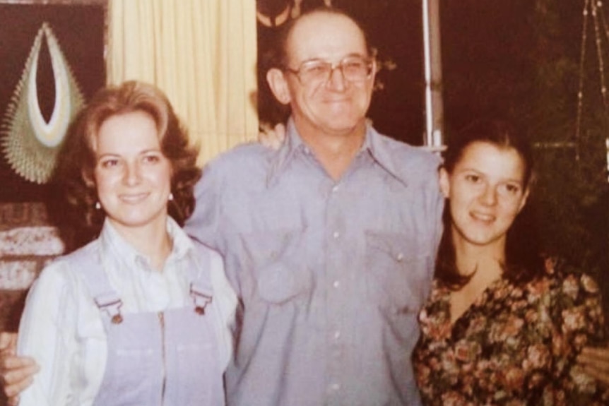 Grainy family photo shows two young women on either side of an older man smiling warmly and wearing glasses.