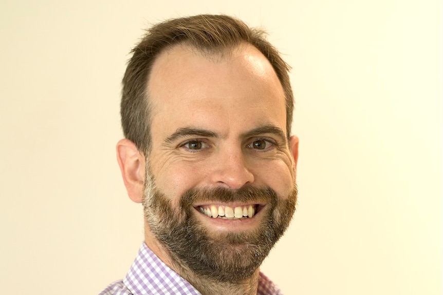A middle aged man with facial hair smiles at camera.