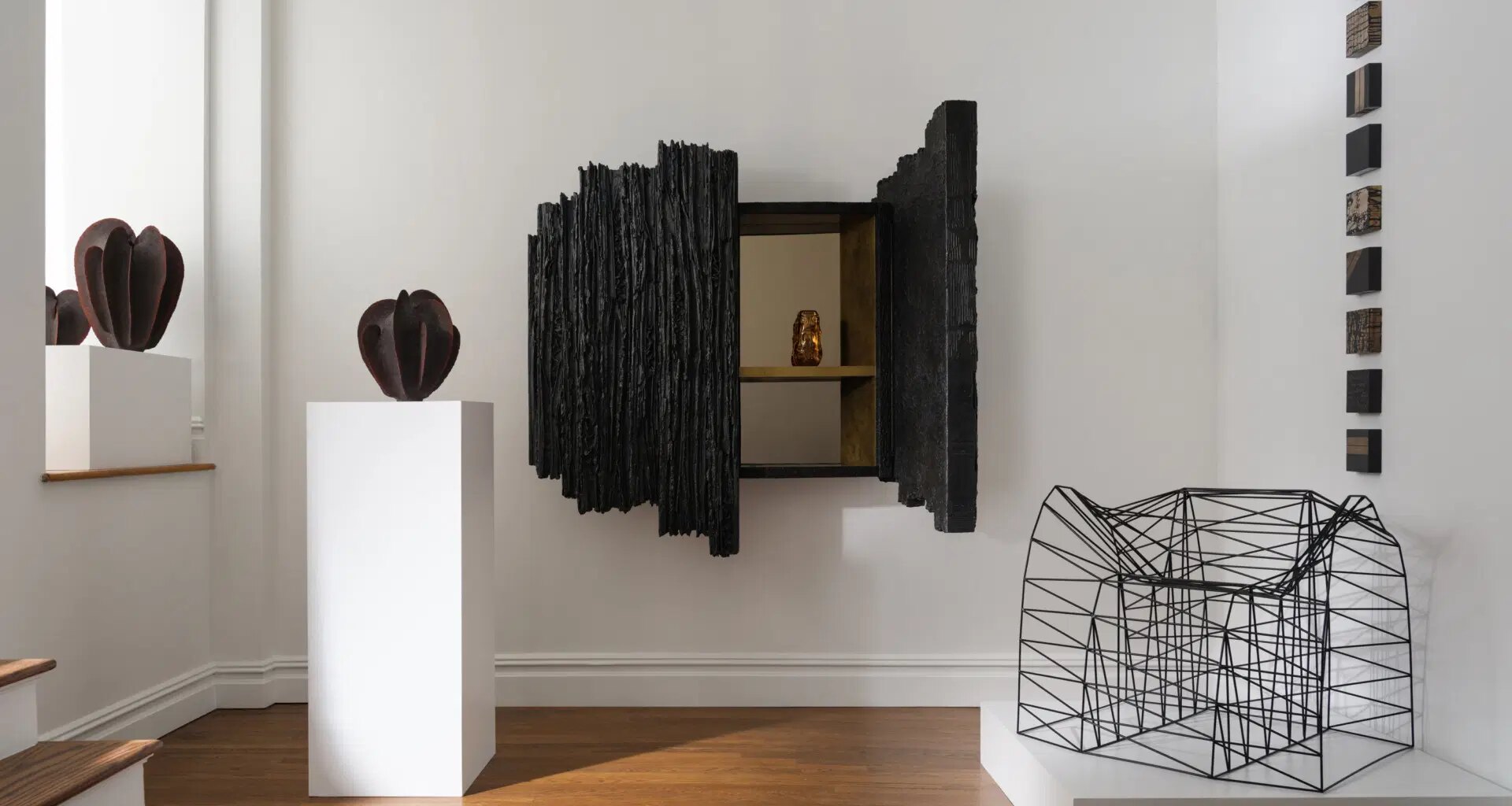 Modern art gallery featuring abstract sculptures and geometric installations in a minimalistic white room with wooden flooring.