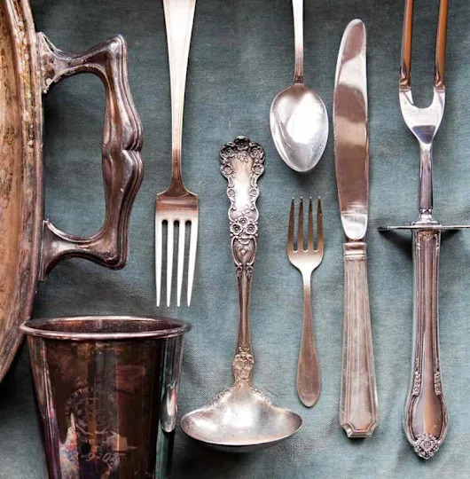 Assorted vintage silverware including forks, spoons, and a ladle on a blue cloth.