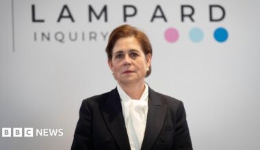 Baroness Kate Lampard wears a black jacket over a white shirt. She stands in front of a white background with the wording "Lampard Inquiry" in black letters, followed by three coloured dots.