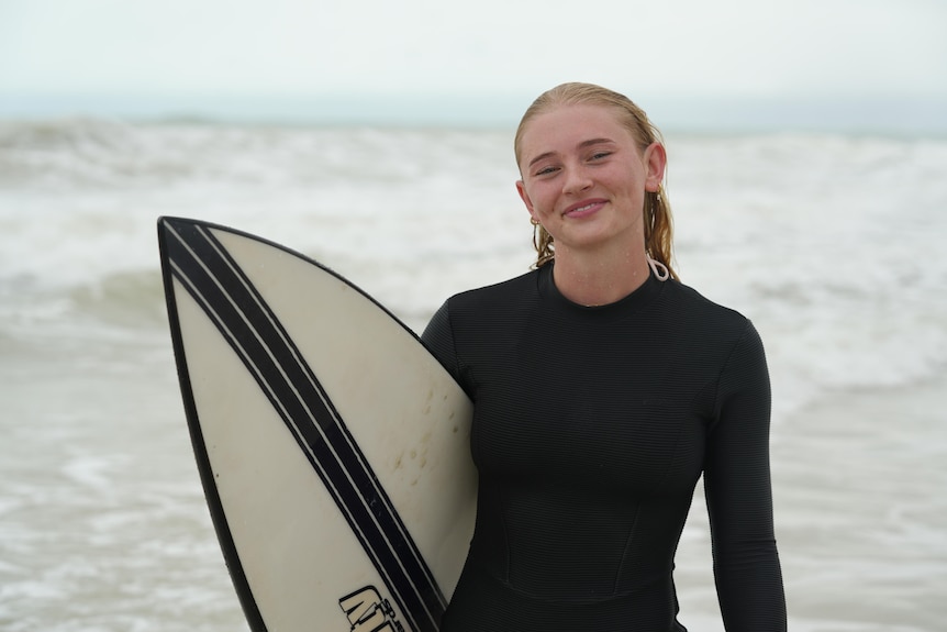 a girl holding a surfboard at the beach.