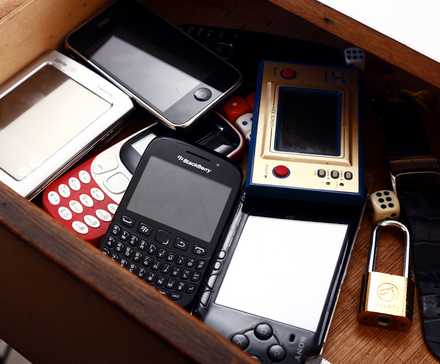 A desk drawer full of old phones and handheld game consoles.