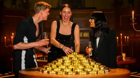 PA Media Rachel, Stephen and Claudia surrounded by golden coins. They are all laughing as they win the money. 