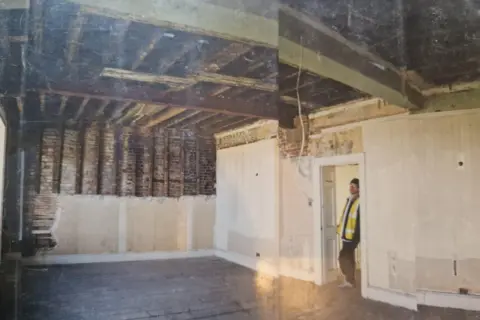 Master Shipwrights House Derelict room with exposed ceiling and a man in doorway wearing high-viz jacket