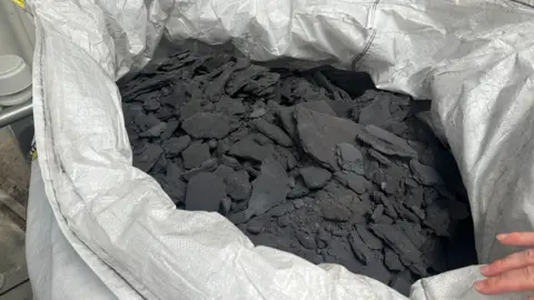 A light-coloured bag containing black material. 