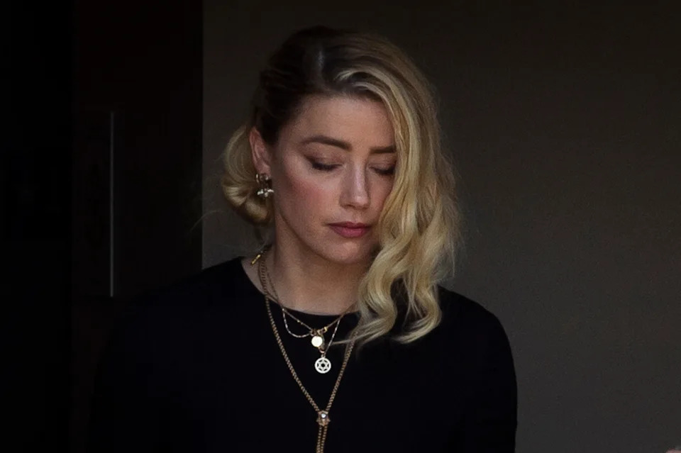 Amber Heard with wavy hair looks down thoughtfully, wearing layered necklaces and a black top