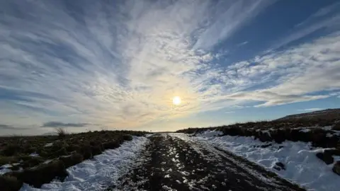 BBC Weather Watcher Fernisky Sun shines out of a blue sky with white clouds over grass ground covered with some white snow in Kells, County Antrim